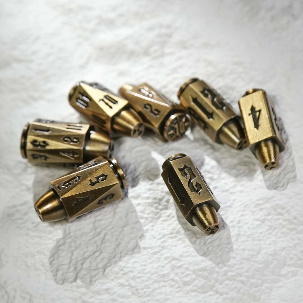 Shaped Polyhedron Metal Bullet Dice Set – Cool antique gold polyhedron DND metal bullet dice set scattered on a white