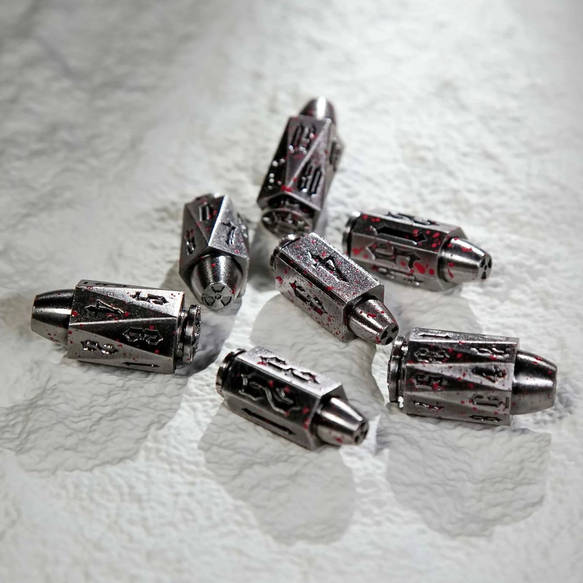 Shaped Polyhedron Metal Bullet Dice Set – A cool blood-stained polyhedron DND metal bullet dice set is scattered on a